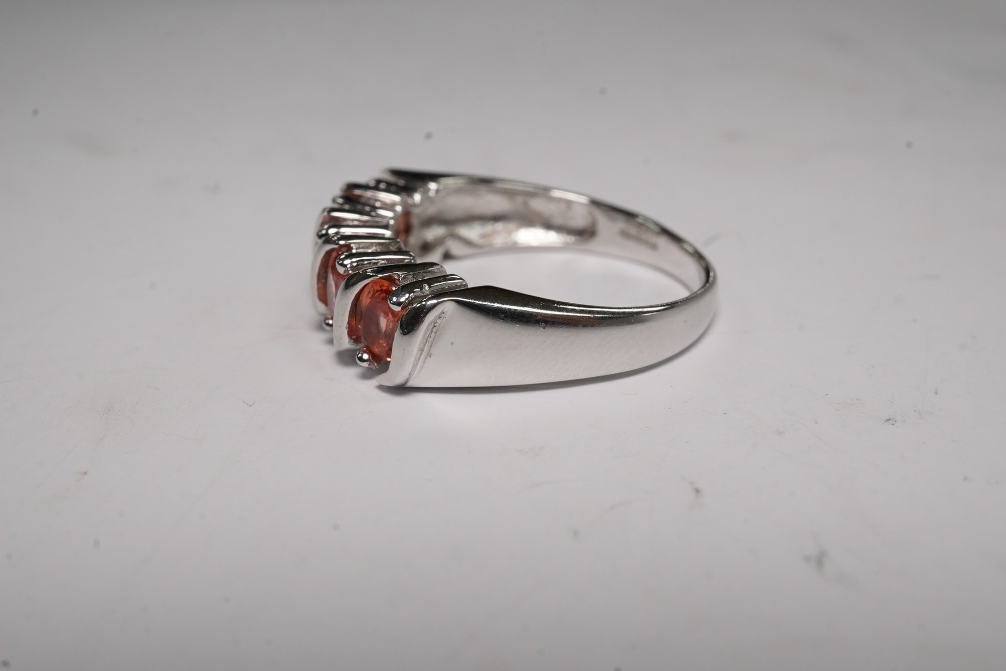 A modern 18ct white gold and five stone orange/pink stone set half hoop ring, size M/N, gross weight 5.6 grams. Condition - fair to good